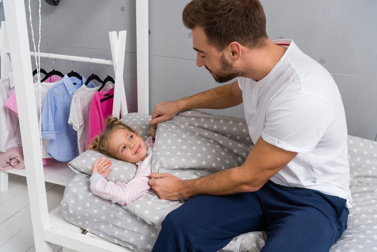 A father sitting on the edge of his young daughter's bed at bedtime