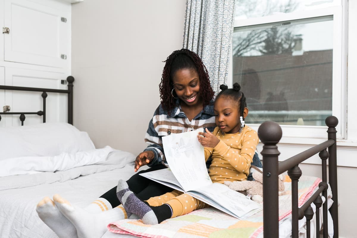 A mother reading a picture book with her young daughter on a bed