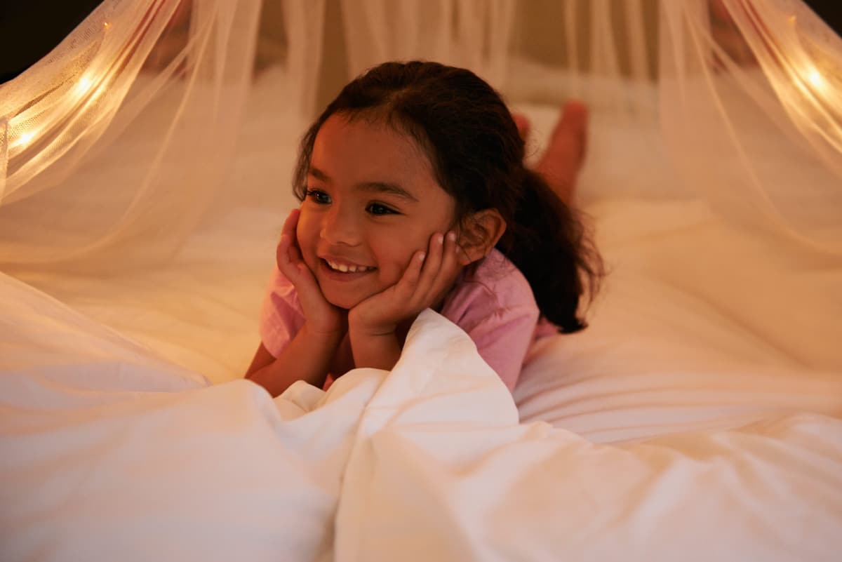 A smiling young girl lying in bed under a canopy of soft lights